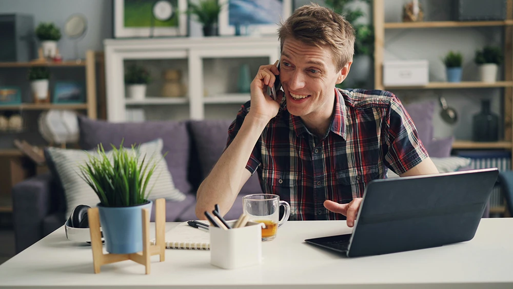 Smiling man working on a laptop and phone for remote customer support jobs in Hungary.