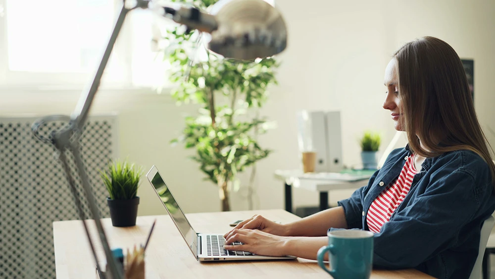 Woman working on a laptop in a green home office for remote jobs in Hungary through Djobzy.